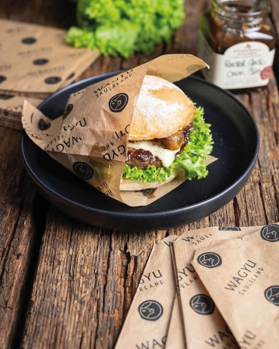 Tüte für den Wagyu-Sauerland Burger auf einem Teller, GARLIC ONION JAM, Burgertüten mit Wagyu Sauerland Branding